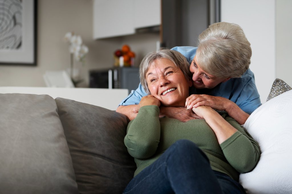 Couple of elderly women embracing over the back of a sofa