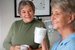 Elderly woman observing another woman with a big smile while drinking a cup of hot beverage