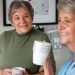 Elderly woman observing another woman with a big smile while drinking a cup of hot beverage